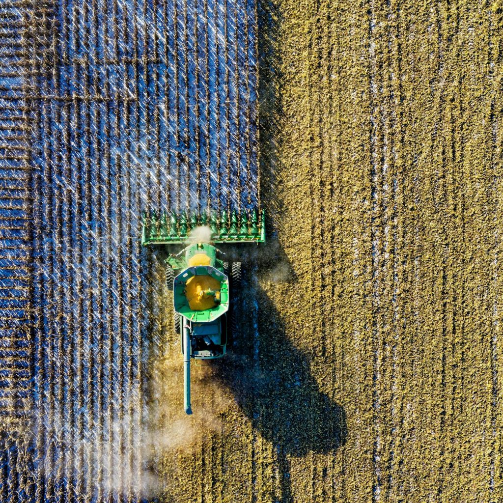 Aerial drone shot of a combine harvester working in a cornfield during harvest season in rural Minnesota.